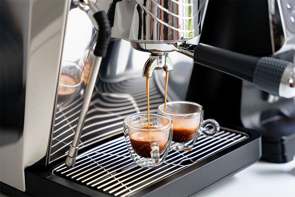 2 Espressotassen stehen in einer Kaffeemaschine und werden von ihr befüllt