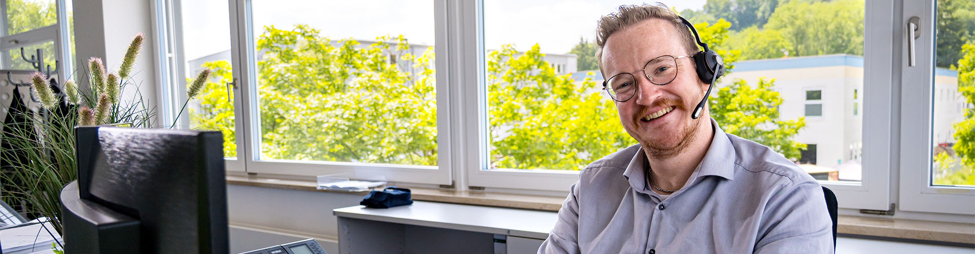 Mitarbeiter sitzt vor seinem Monitor am Schreibtisch und lächelt